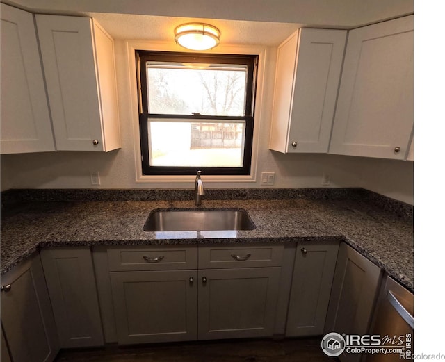 kitchen featuring dark stone countertops, sink, and white cabinets