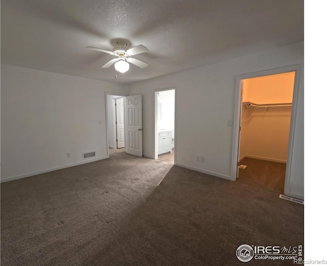 unfurnished bedroom featuring ensuite bathroom, a spacious closet, ceiling fan, and dark carpet