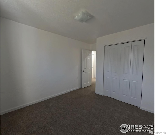 unfurnished bedroom with dark colored carpet and a closet