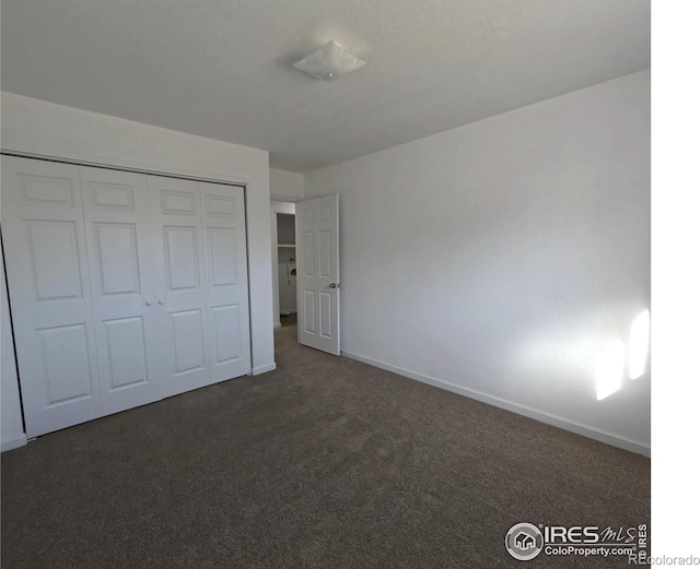 unfurnished bedroom with dark colored carpet and a closet