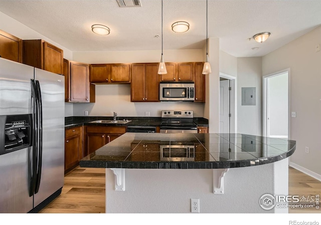 kitchen featuring sink, stainless steel appliances, light hardwood / wood-style flooring, decorative light fixtures, and a breakfast bar area