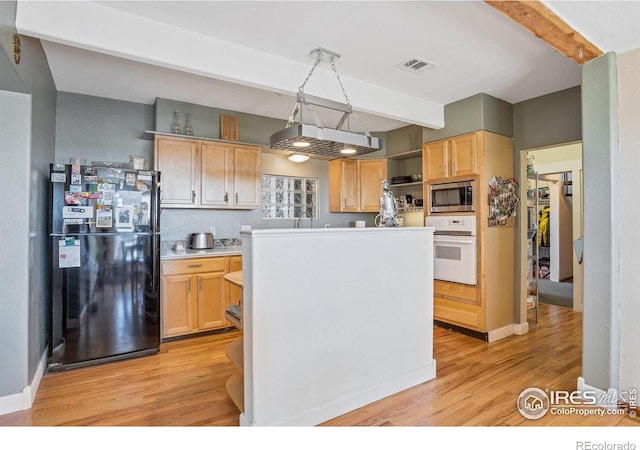 kitchen with black refrigerator, light brown cabinets, white oven, and stainless steel microwave