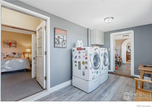 clothes washing area with washer and dryer, light hardwood / wood-style floors, and cabinets