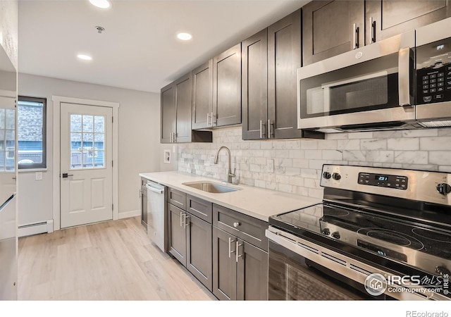 kitchen with light wood-type flooring, backsplash, stainless steel appliances, baseboard heating, and sink