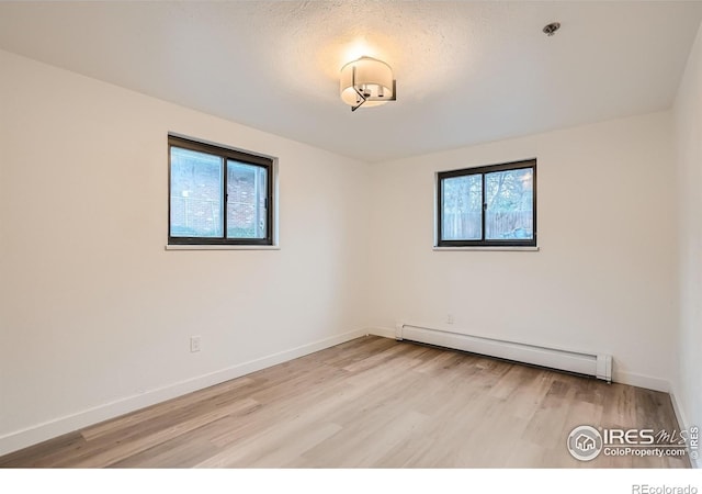 spare room featuring a baseboard radiator, a textured ceiling, and light wood-type flooring