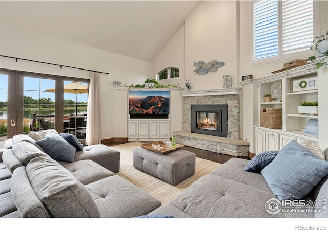 living room featuring light wood-type flooring, high vaulted ceiling, a healthy amount of sunlight, and a stone fireplace