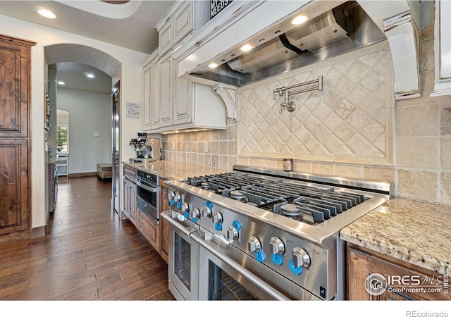 kitchen featuring premium range hood, light stone countertops, tasteful backsplash, dark hardwood / wood-style flooring, and stainless steel appliances