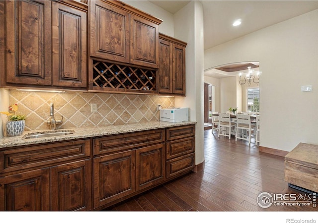 kitchen featuring backsplash, an inviting chandelier, sink, dark hardwood / wood-style floors, and light stone countertops