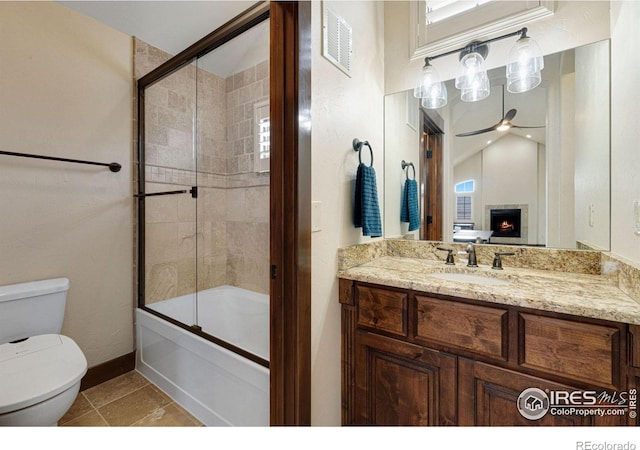 full bathroom featuring ceiling fan, a large fireplace, tile patterned flooring, toilet, and shower / bath combination with glass door