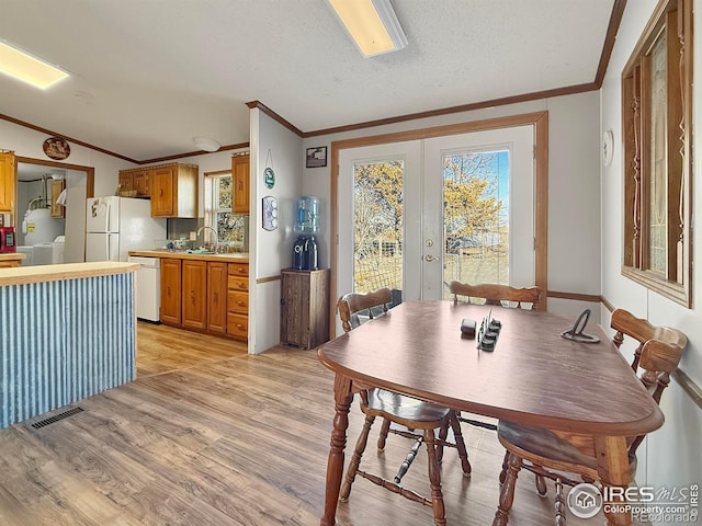 dining space featuring french doors, sink, light wood-type flooring, a textured ceiling, and ornamental molding