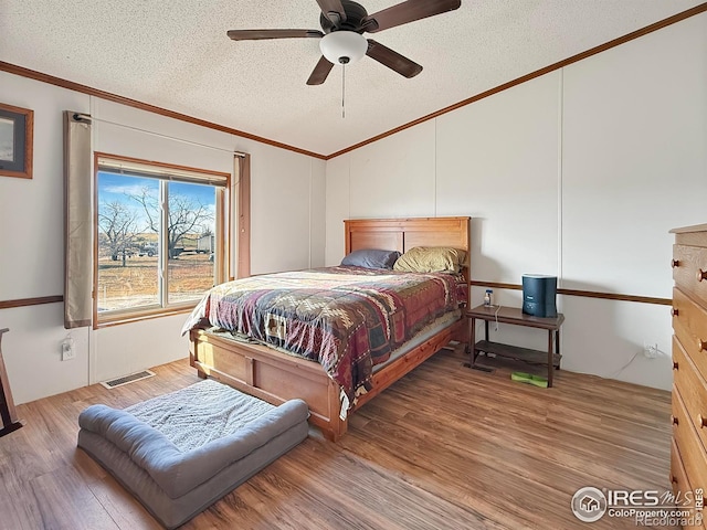 bedroom with ceiling fan, ornamental molding, a textured ceiling, and hardwood / wood-style flooring