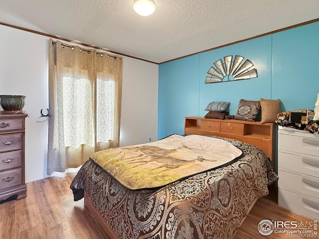 bedroom with crown molding, a textured ceiling, and light wood-type flooring