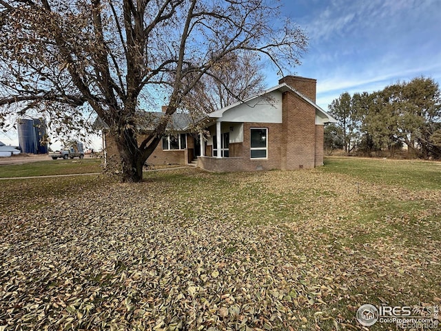 view of front of home featuring crawl space, brick siding, a chimney, and a front yard