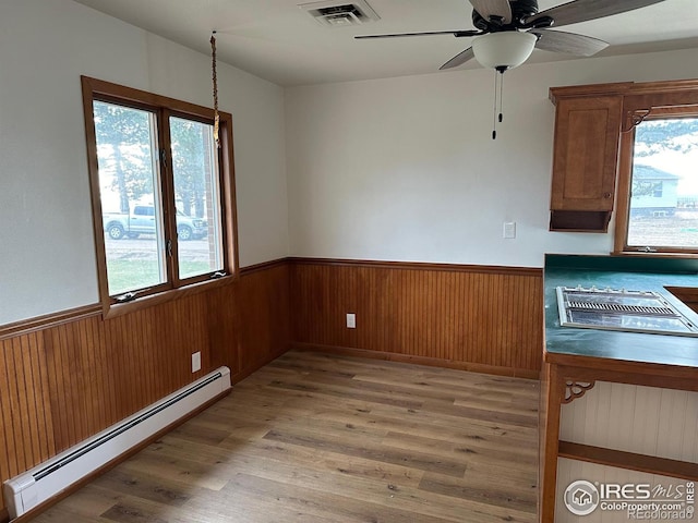 unfurnished dining area featuring wainscoting, a wealth of natural light, a baseboard radiator, and visible vents