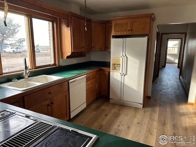 kitchen with white appliances, dark countertops, brown cabinets, light wood-style floors, and a sink