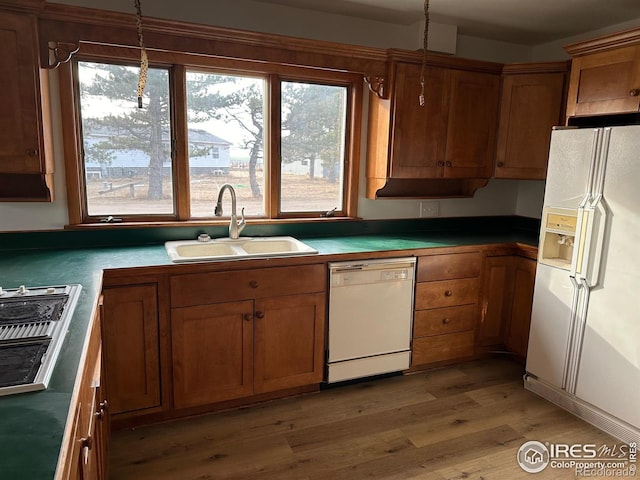 kitchen featuring light wood-style flooring, white appliances, a sink, hanging light fixtures, and brown cabinetry