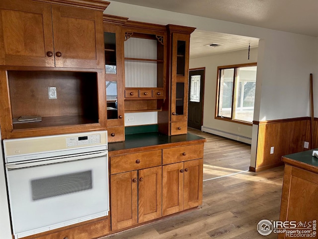 kitchen featuring oven, a baseboard heating unit, a wainscoted wall, light wood finished floors, and brown cabinetry