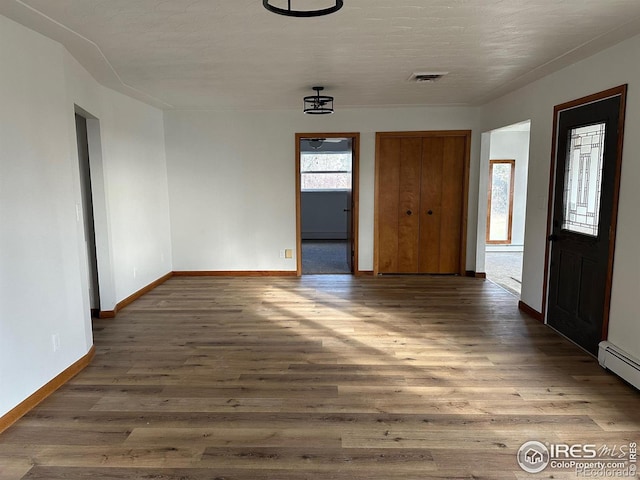 interior space with a baseboard heating unit, visible vents, baseboards, and wood finished floors