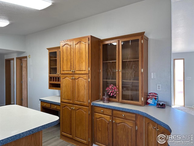 kitchen with brown cabinets, light wood finished floors, light countertops, glass insert cabinets, and a textured ceiling