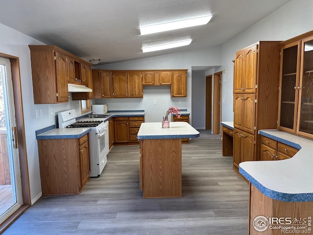 kitchen with under cabinet range hood, white range with gas stovetop, a kitchen island, vaulted ceiling, and brown cabinetry