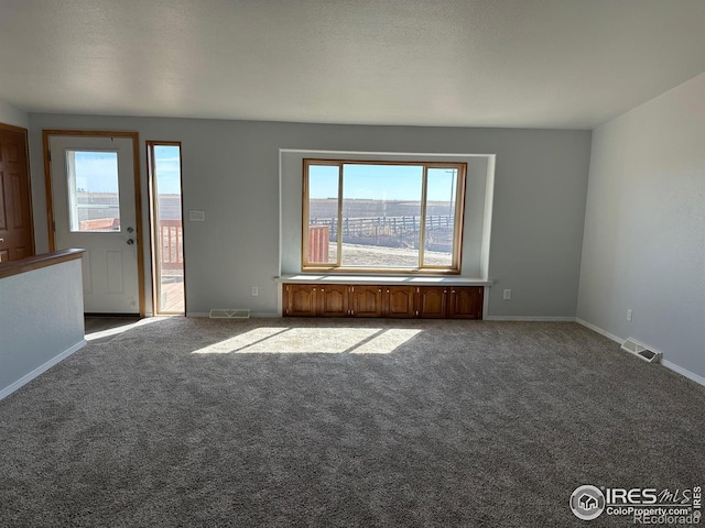 carpeted empty room with visible vents, a textured ceiling, and baseboards