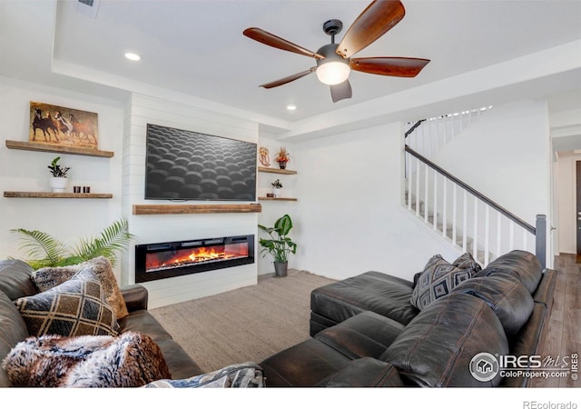 living room featuring hardwood / wood-style floors, a large fireplace, a raised ceiling, and ceiling fan