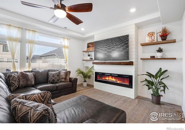 living room with a tray ceiling, ceiling fan, a large fireplace, and wood-type flooring