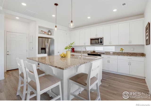 kitchen featuring pendant lighting, a kitchen island with sink, white cabinets, light wood-type flooring, and stainless steel appliances