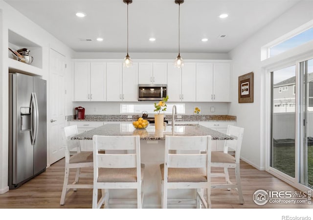 kitchen featuring an island with sink, white cabinets, pendant lighting, and appliances with stainless steel finishes