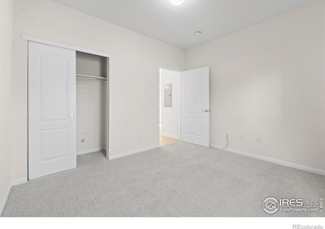 unfurnished bedroom with a closet, electric panel, carpet flooring, and baseboards