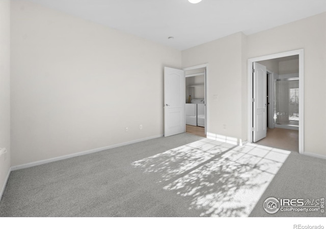 unfurnished bedroom featuring baseboards, separate washer and dryer, carpet flooring, and ensuite bathroom