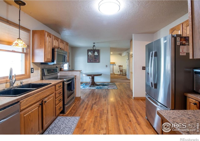 kitchen with sink, hanging light fixtures, light wood-type flooring, and appliances with stainless steel finishes