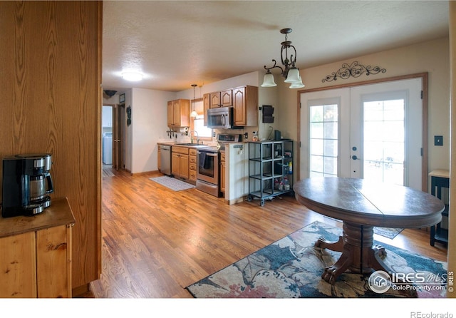 kitchen with sink, french doors, stainless steel appliances, pendant lighting, and light hardwood / wood-style floors