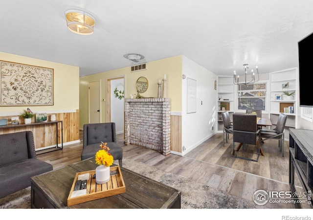 living room featuring wood-type flooring, wooden walls, built in features, and a notable chandelier