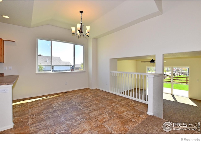 empty room with lofted ceiling, stone finish flooring, baseboards, and ceiling fan with notable chandelier