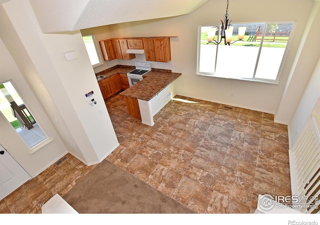 kitchen with white electric range oven, dark countertops, brown cabinets, a peninsula, and stone finish flooring