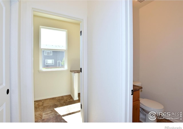 bathroom featuring stone finish flooring, vanity, toilet, and baseboards