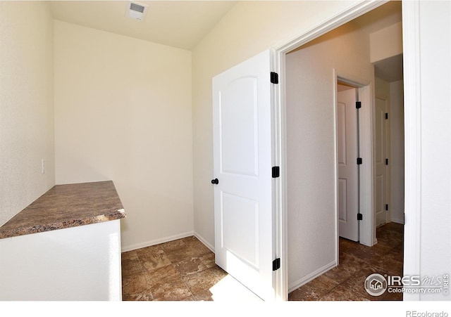 corridor featuring stone finish floor, baseboards, and visible vents