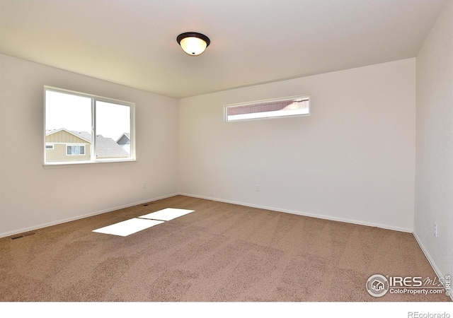 carpeted spare room featuring visible vents, baseboards, and a wealth of natural light