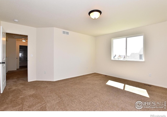 spare room with carpet floors, visible vents, and baseboards