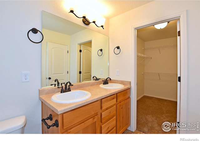 bathroom with a walk in closet, a sink, toilet, and double vanity