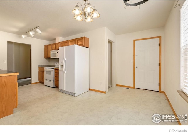 kitchen with white appliances, a healthy amount of sunlight, rail lighting, and a notable chandelier