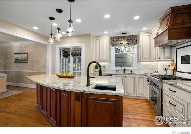 kitchen featuring a kitchen island with sink, high end stainless steel range, sink, and light wood-type flooring