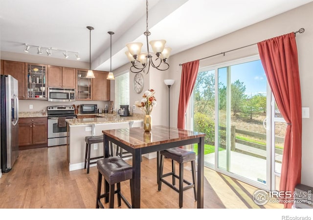 kitchen featuring a breakfast bar area, hanging light fixtures, kitchen peninsula, stainless steel appliances, and light stone countertops