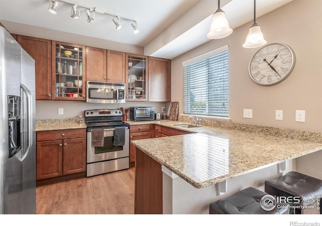 kitchen featuring stainless steel appliances, hanging light fixtures, glass insert cabinets, a sink, and a peninsula