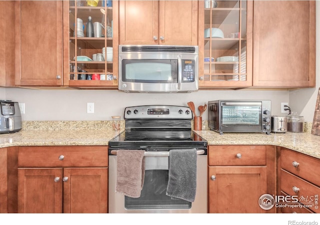 kitchen featuring stainless steel appliances, a toaster, glass insert cabinets, and light stone counters