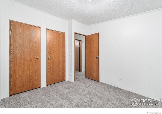 unfurnished bedroom with a textured ceiling, light colored carpet, and multiple closets