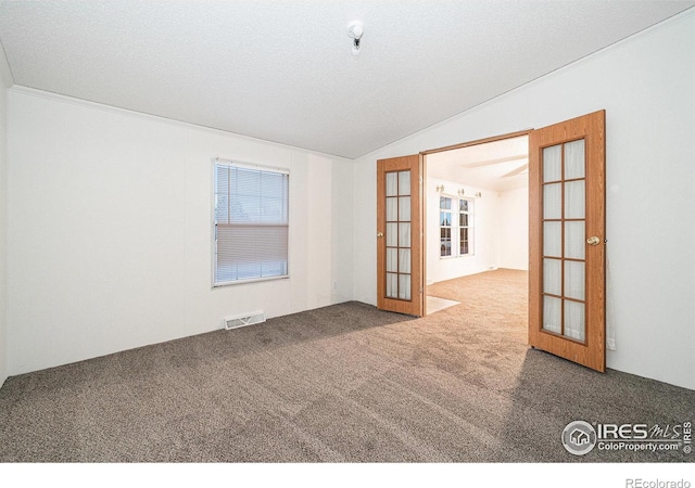 carpeted empty room featuring french doors, a textured ceiling, and lofted ceiling