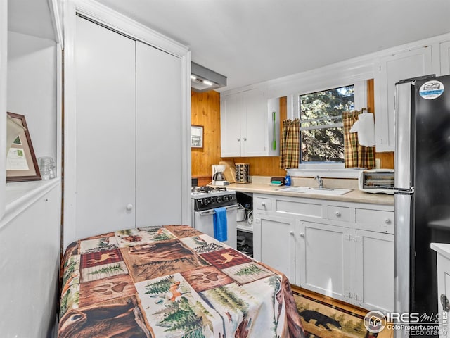 kitchen featuring white range with gas cooktop, exhaust hood, sink, white cabinets, and stainless steel refrigerator