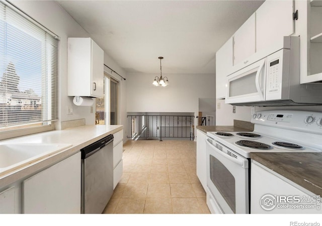 kitchen with a notable chandelier, a wealth of natural light, white appliances, white cabinetry, and hanging light fixtures